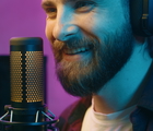Smiling man in headphones speaking into a microphone with colorful lighting background.